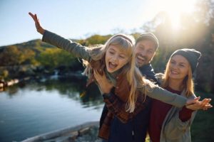 Happy family moment with dad carrying the child like flying and mom smiling nearby.