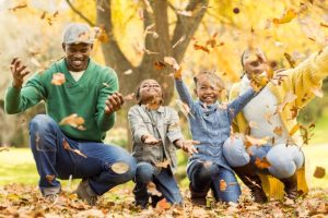 Joyful family enjoying a playful moment in the park with autumn leaves falling around them.