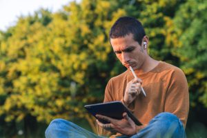 Young adult man using a tablet and pen for studying outdoors in a park setting